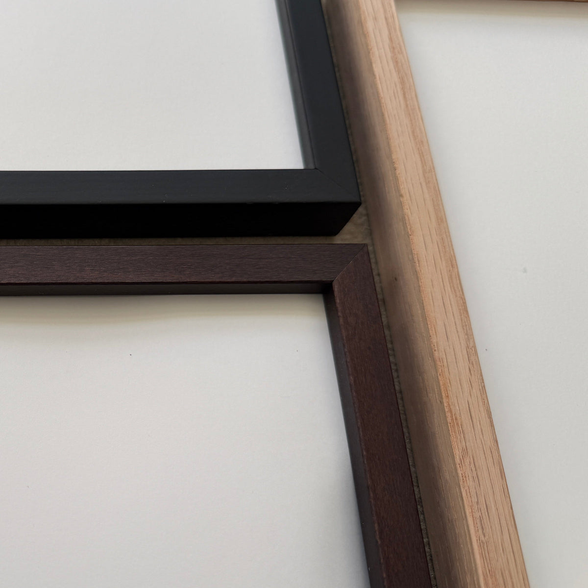 Two empty picture frames mounted on a light wood shelf against a white wall, one in dark brown wood and one in black wood.