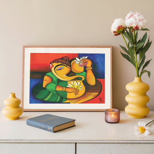 A framed colorful art print of Ganesha on a white console table, styled with a yellow vase of flowers, a small yellow vase, a book, and a lit candle against a beige wall.